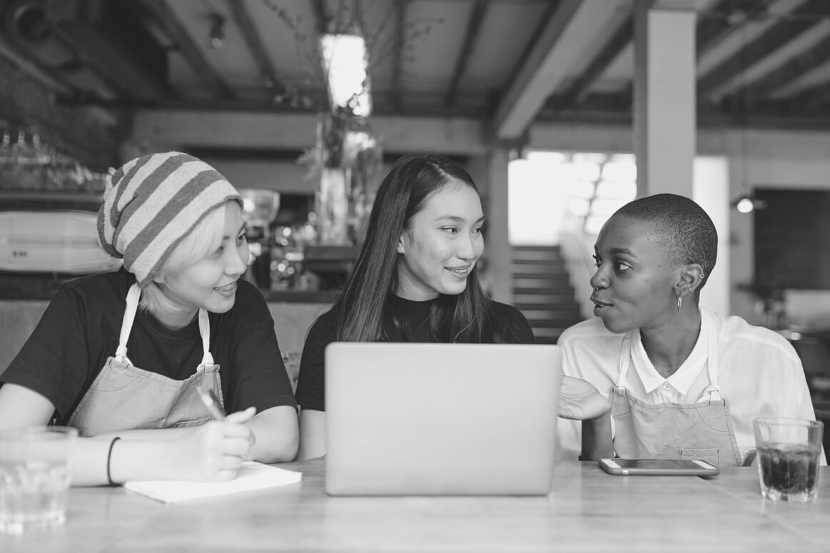 Positive diverse coworkers chatting and sitting at table with laptop